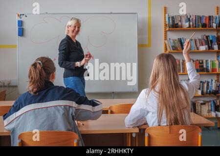 Due studentesse delle scuole superiori partecipano attivamente alla classe, volendo rispondere alle domande e alzare la mano Foto Stock