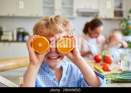 Ragazzo felice che copre il viso con fette di arance fresche in cucina a casa Foto Stock