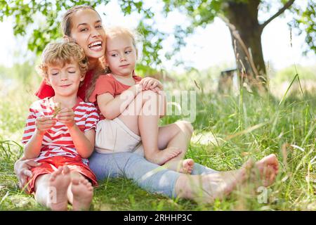 Ritratto di una donna felice che si diverte con figlio e figlia seduto in giardino Foto Stock
