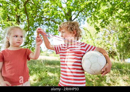 Fratello che mostra la medaglia alla sorella mentre tiene la palla da calcio in giardino Foto Stock