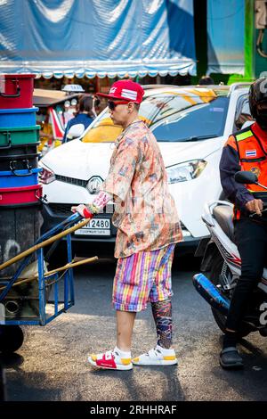 Un operaio del mercato tailandese si fa strada attraverso la trafficata Yaowarat Rd. China Town, Bangkok, Thailandia. Foto Stock