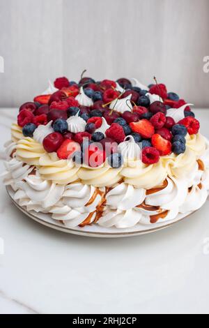 Pavlova Berry cake con salsa al caramello salata, lamponi ripieni, fragole, ciliegie e mirtilli su sfondo grigio neutro Foto Stock