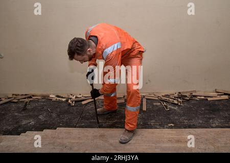 Pavimenti in legno rimozione del parquet da parte del costruttore, indossando guanti, stivali e tute arancioni. Foto Stock