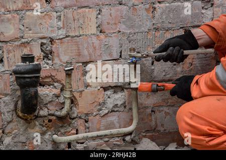 Serraggio della valvola dell'acqua che perde indossando guanti e tute arancioni. Foto Stock