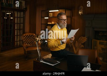 Uomo maturo concentrato e impegnato che legge il rapporto mentre lavora a casa Foto Stock