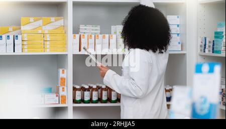 La giovane e concentrata farmacista usa il suo tablet per fare le scorte in una moderna farmacia. Multietnico lavoratore professionista della salute femminile o. Foto Stock