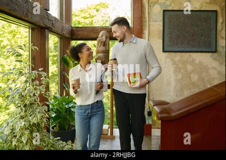Colleghi multietnici che fanno una pausa caffè passeggiando in un ufficio ecologico Foto Stock