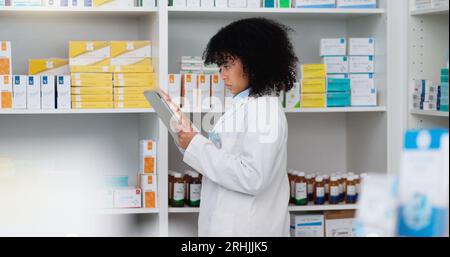 La giovane e concentrata farmacista usa il suo tablet per fare le scorte in una moderna farmacia. Multietnico lavoratore professionista della salute femminile o. Foto Stock