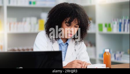 Una giovane farmacista che usa il suo computer per fare stock taking e dispensare medicine in farmacia o farmacia. Professionista sanitario femminile o. Foto Stock