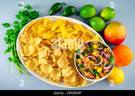 Ceviche di salmone con mango servito con patatine fritte e tortilla: Una ciotola di ceviche di salmone e mango con patatine fritte circondate da ingredienti Foto Stock