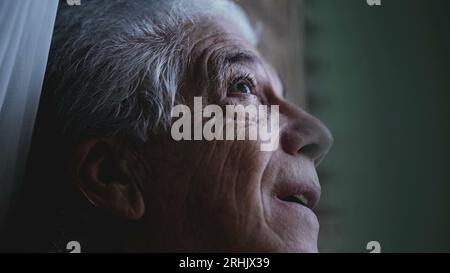 L'uomo anziano guarda da vicino il cielo dalla finestra di casa, osservando il tempo e la pioggia in arrivo. Persona anziana che fissa la formazione della tempesta Foto Stock