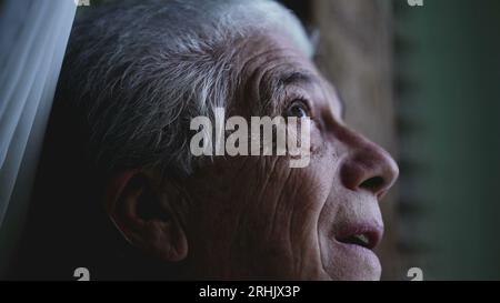 L'uomo anziano guarda da vicino il cielo dalla finestra di casa, osservando il tempo e la pioggia in arrivo. Persona anziana che fissa la formazione della tempesta Foto Stock