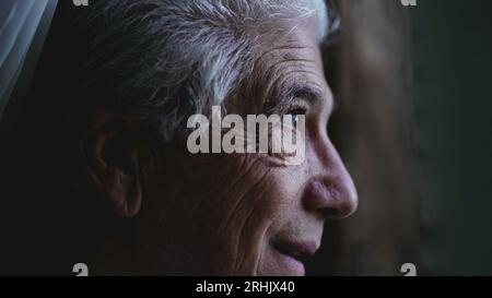 L'uomo anziano guarda da vicino il cielo dalla finestra di casa, osservando il tempo e la pioggia in arrivo. Persona anziana che fissa la formazione della tempesta Foto Stock