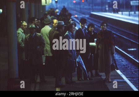 Pendolari in treno la mattina presto, al crepuscolo, in attesa di un treno alla stazione ferroviaria di Grantham per raggiungere Londra. Un uomo d'affari cittadino indossa un cappello da soffiatore. 1980s Lincolnshire, Inghilterra Regno Unito HOMER SYKES Foto Stock