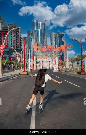 Sullo sfondo della Coppa del mondo FIFA 2022 in Qatar, un tifoso scivola con grazia sulle sue scarpe da pattinaggio lungo la strada adiacente al vivace Cor Foto Stock