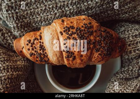 Una tazza di caffè nero del mattino con un croissant al cioccolato. Pasto delizioso. Estetica nei dettagli. Tonalità accoglienti beige e marrone Foto Stock