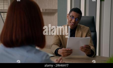 Sorridente uomo d'affari afroamericano datore di lavoro parlare con la donna che assume un candidato colloquio di lavoro riprendere il reclutamento di lavoro sul posto di lavoro ascoltare Foto Stock