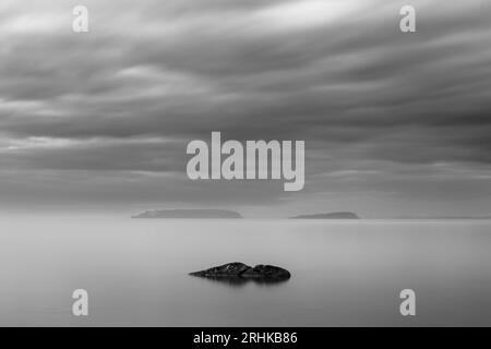 Vista a lunga esposizione di una roccia nel lago Trasimeno dell'Umbria, con isole sullo sfondo e cielo lungoso Foto Stock