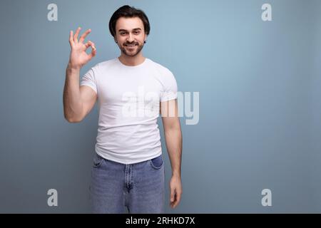 giovane bruna, sicuro di sé, con t-shirt bianca e jeans, mostra un gesto della mano discreto Foto Stock