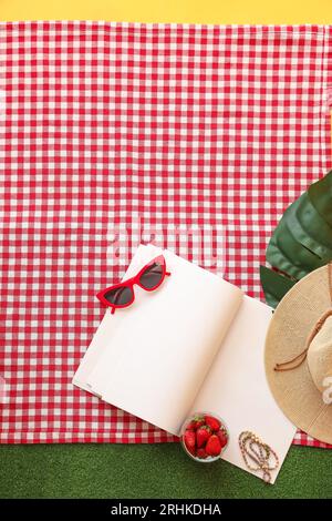 Fragole fresche da picnic con notebook vuoto e accessori da spiaggia su quadri rossi a scacchi. Concetto di vacanza estiva Foto Stock