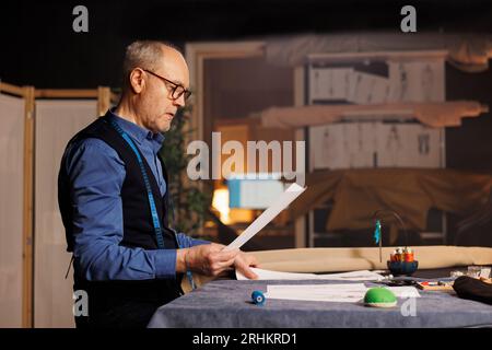 Sartoria che guarda i disegni degli schizzi, si prepara a produrre capi sartoriali per il cliente. Stilista di moda che concettualizza gli outfit seguendo le bozze di abbigliamento fatte su misura Foto Stock