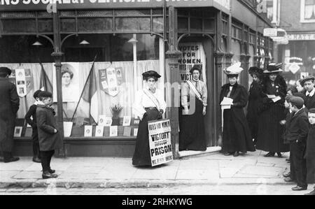 Kensington Women's Social & Political Union, Mary Sinclair all'esterno del negozio con poster "Victory Through Prison" insieme a bambini e altre suffragette, volantini, bandiere e un'immagine di Emmeline Pankhurst nella vetrina del negozio Foto Stock