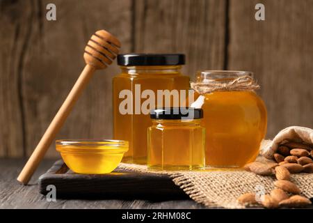 Composizione creativa di miele in un vaso di vetro e una ciotola, un cucchiaio di legno e fiori gialli su uno sfondo di legno invecchiato. Il concetto di ape organica Foto Stock