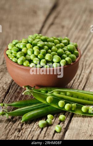 Piselli sbucciati in un recipiente di argilla, piselli verdi biologici dolci in cialde chiuse e aperte e grani sparsi su uno sfondo di legno invecchiato. Foto Stock