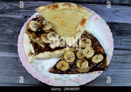 Un piatto di dessert con Una dolce pasticceria di pizza al cioccolato, Chakhtoura, dolce pasticceria al forno, ricoperta di cioccolato, fette di banana, l Foto Stock