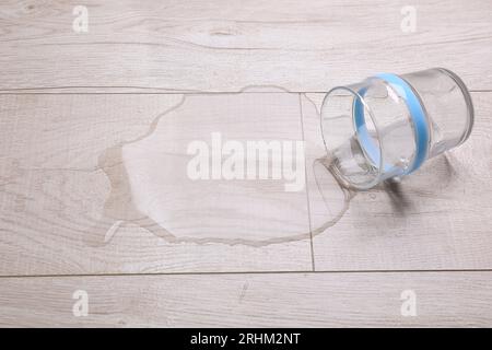 Vetro con acqua versata su pavimento in legno Foto Stock