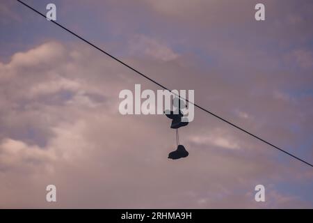 Le sneaker Old garland sono appese a un filo elettrico contro il cielo e le nuvole. Cultura moderna degli adolescenti. Foto Stock