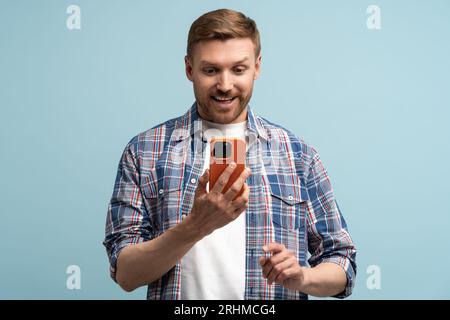 L'uomo con lo smartphone sorride felicemente, guarda lo schermo. Buone notizie, sorpresa, messaggio gioioso Foto Stock