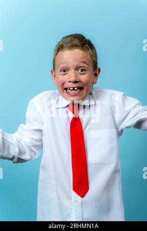 un primo elementare felice e divertente in una camicia bianca con una cravatta rossa sta ridendo. Carino ragazzo caucasico va a scuola. Scolaro. Il 1° settembre, per la prima volta Foto Stock