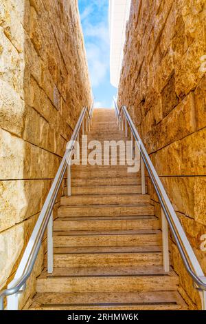 Salendo i gradini all'interno di uno stretto passaggio tra due pareti di pietra che conducono verso il vivace cielo blu Foto Stock
