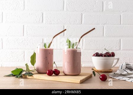 Due eleganti bicchieri con frullati di ciliegia appena fatti e una ciotola di ciliegie mature sulla tavola di legno. Una bevanda deliziosa e salutare. Disintossicazione Foto Stock