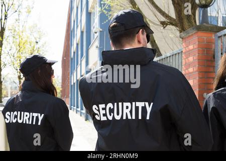Vista posteriore di guardie di sicurezza in uniforme nera in piedi fuori dall'edificio Foto Stock