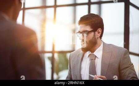 Un uomo d'affari prende un partner nel suo ufficio seduto al tavolo Foto Stock