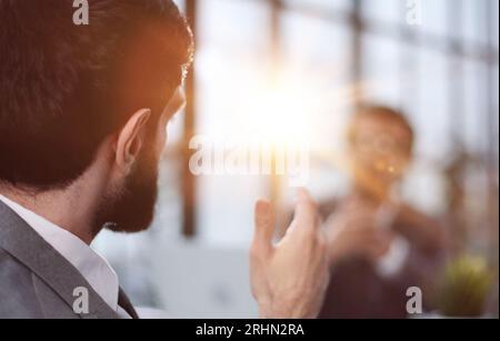 Un giovane si siede con le spalle alla telecamera a un tavolo in un ufficio. Vista dal retro Foto Stock