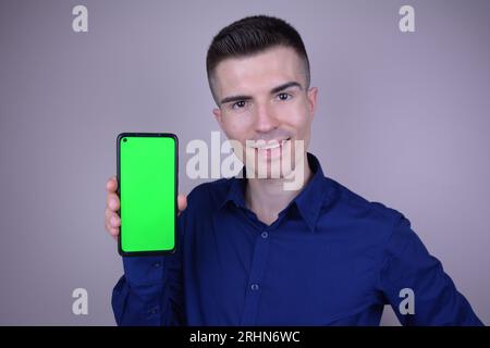 Elegante giovane bel sorridente uomo caucasico tenendo smartphone con schermo verde Foto Stock