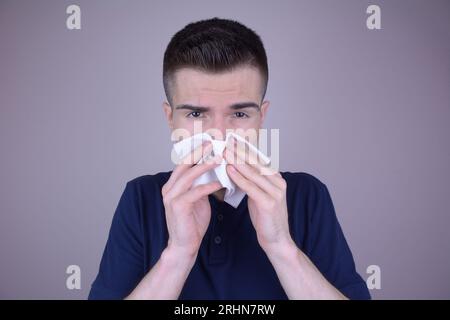 Giovane uomo caucasico con naso che cola utilizza tessuto a causa del freddo su sfondo isolato Foto Stock