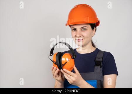 Lavoratore edile femminile in elmetto protettivo che regge le cuffie su sfondo bianco. Foto Stock
