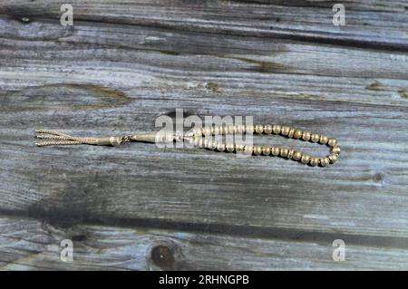 Piccolo rosario islamico di colore argento con 33 perle di rosario isolate su sfondo di legno, i musulmani lo usano per elogiare Allah usando frasi agli uomini Foto Stock