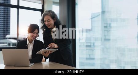 Mentore, coaching o donne d'affari con tablet che parlano, parlano o pianificano un progetto in ufficio. Tecnologia, collaborazione di gruppo senior manager Foto Stock