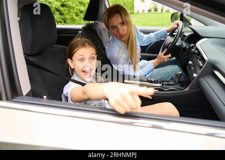 La bambina felice sta puntando qualcosa fuori dal finestrino dell'auto Foto Stock