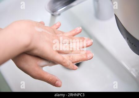 La donna si lava le mani saponate sotto l'acqua corrente Foto Stock