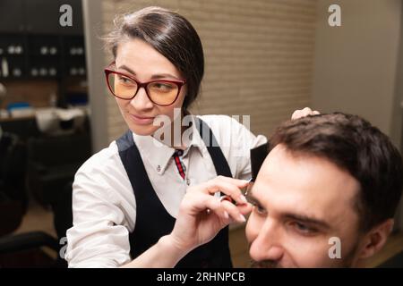 Femmina con occhiali taglia i capelli dei clienti con le forbici Foto Stock