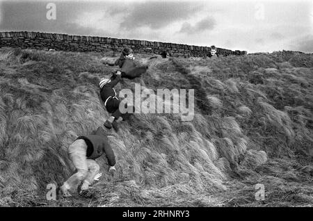 Bambini degli anni '1960 che giocano con un gruppo di ragazzi, amici che giocano giù per una banca erbosa campagna dello Yorkshire Inghilterra 1968 UK HOMER SYKES Foto Stock