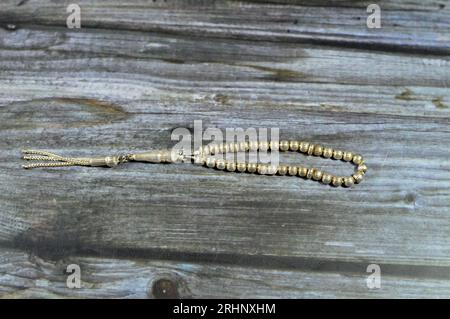 Piccolo rosario islamico di colore argento con 33 perle di rosario isolate su sfondo di legno, i musulmani lo usano per elogiare Allah usando frasi agli uomini Foto Stock