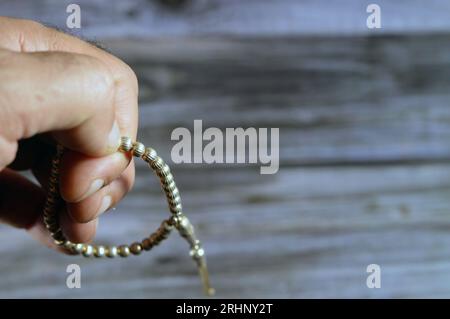 Piccolo rosario islamico di colore argento con 33 perle di rosario isolate su sfondo di legno, i musulmani lo usano per elogiare Allah usando frasi agli uomini Foto Stock