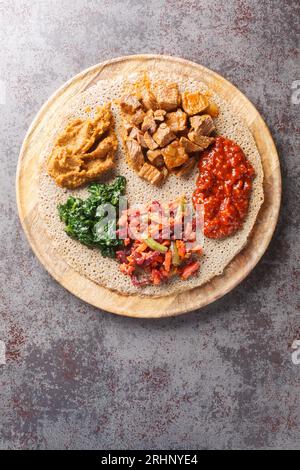 I pasti consistenti in injera e diversi tipi di stufato wat o tsebhi sono tipici della cucina etiope primo piano sulla tavola di legno. Vista superiore verticale da Foto Stock